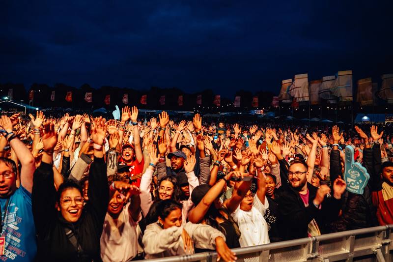 A packed crowd at the front barrier with hands raised at night
