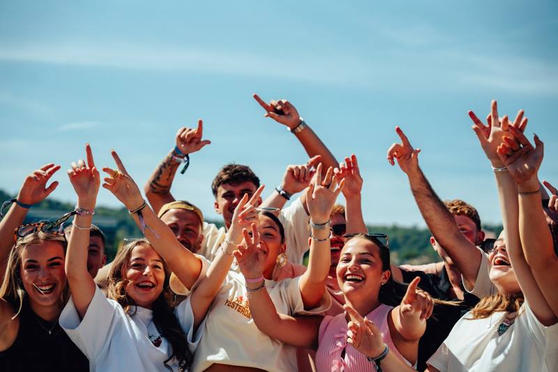 Young people in the crowd dancing with hands in the air on a sunny afternoon